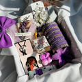 Gift box with purple and white items including a bow, candles, and decorative items