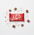 KitKat chocolate bar packaging with scattered chocolate pieces on a white background