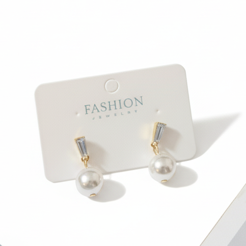Gold earrings on a white card with a light blue fabric 